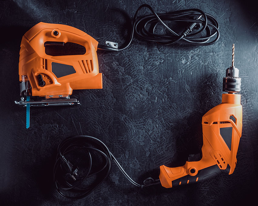 Orange electric saw and drill on dark background.