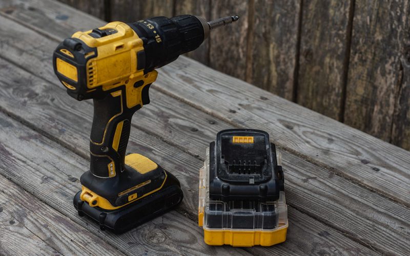 Cordless drill and battery on wooden table.