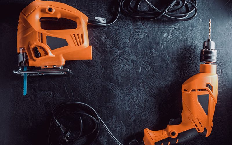 Orange electric saw and drill on dark background.