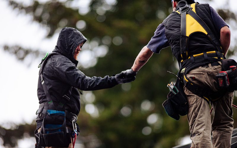 Two men wearing safety gear during rain on rooftop.