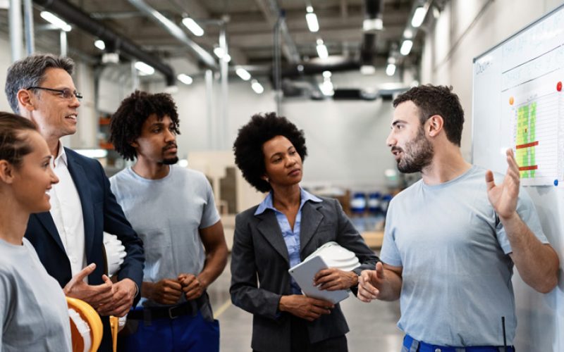 Educator teaching power tool safety to a group of factory workers.
